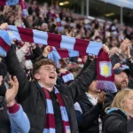Een collectieve groep Aston Villa-supporters viert uitbundig in de tribune.