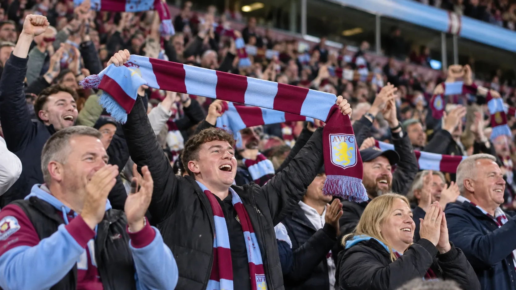Een collectieve groep Aston Villa-supporters viert uitbundig in de tribune.