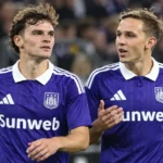 Twee voetballers in paarse wedstrijdshirts op het veld van een stadion.