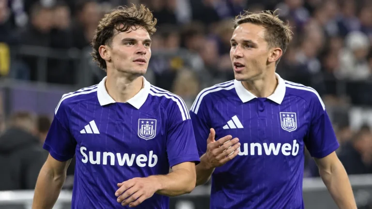 Twee voetballers in paarse wedstrijdshirts op het veld van een stadion.