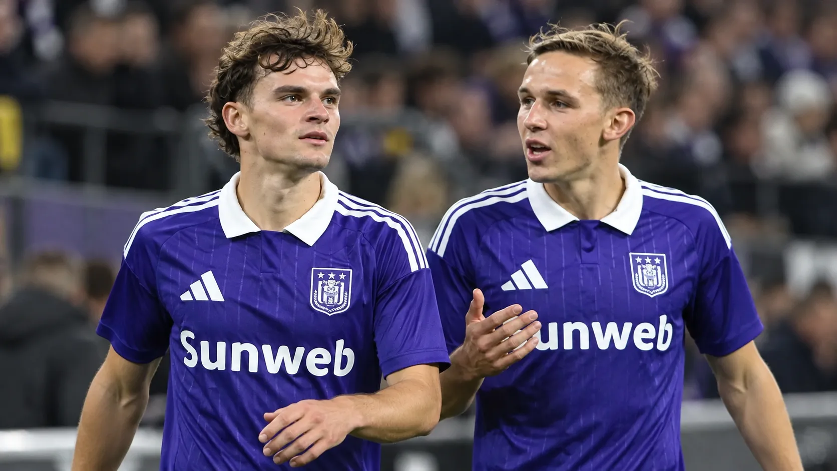Twee voetballers in paarse wedstrijdshirts op het veld van een stadion.