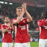 Spelers in rode wedstrijdtenues applaudisseren na afloop op het veld in de regen.