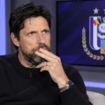 Johan Boskamp zit als analist in een voetbalstudio met een RSC Anderlecht-embleem op een monitor.