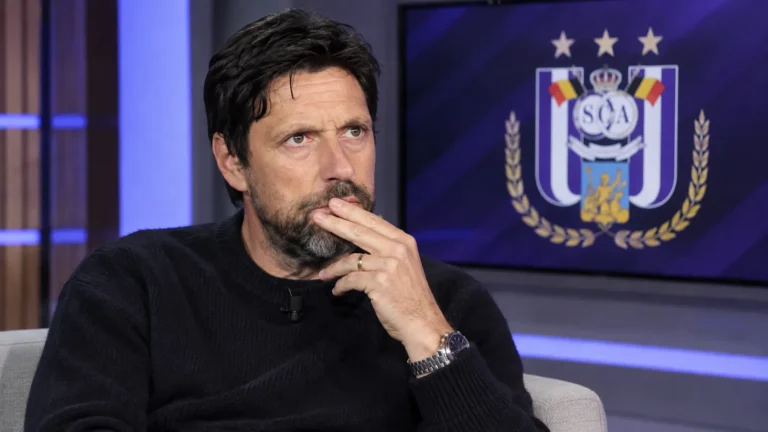 Johan Boskamp zit als analist in een voetbalstudio met een RSC Anderlecht-embleem op een monitor.