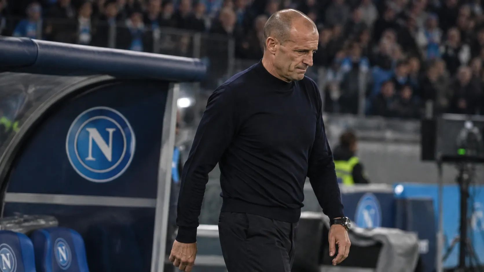 Massimiliano Allegri loopt gespannen langs de technische zone naast een Napoli-paneel op de dug-out.