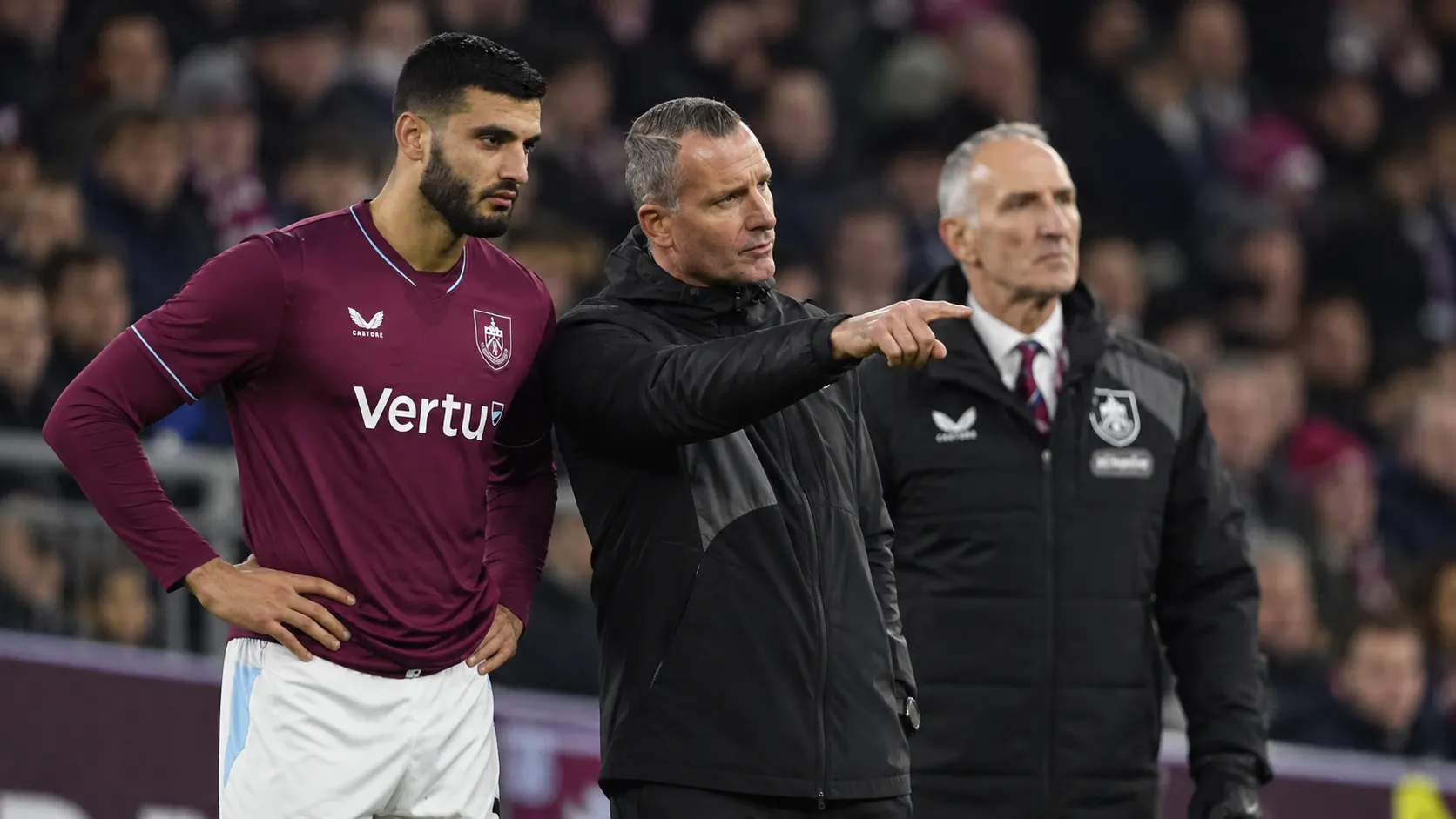 Een Burnley-speler naast twee leden van de staf aan de zijlijn.