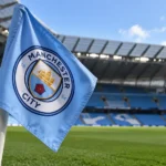 Een lichtblauwe Manchester City-hoekvlag naast het veld in een leeg stadion.