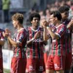 Een groep voetballers in gestreepte wedstrijdshirts applaudisseert naast het veld.