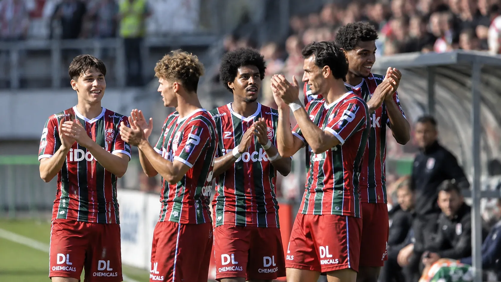 Een groep voetballers in gestreepte wedstrijdshirts applaudisseert naast het veld.