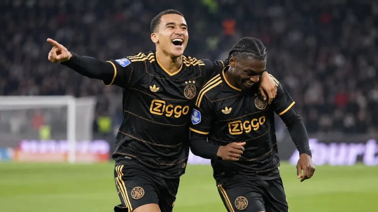 Twee Ajax-spelers in zwart-gouden wedstrijdtenue tijdens een nieuw actiemoment op het veld.