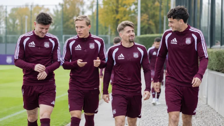Een groep Anderlechtspelers in bordeaux trainingskleding op een trainingsveld.