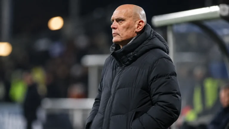 Jürgen Streppel in een donkere jas langs de zijlijn van een voetbalveld.