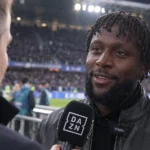Een voormalige voetballer geeft in een stadion een interview met een microfoon.