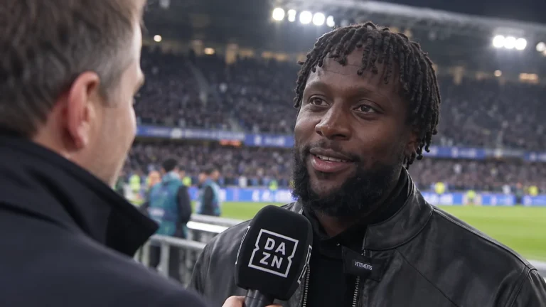 Een voormalige voetballer geeft in een stadion een interview met een microfoon.