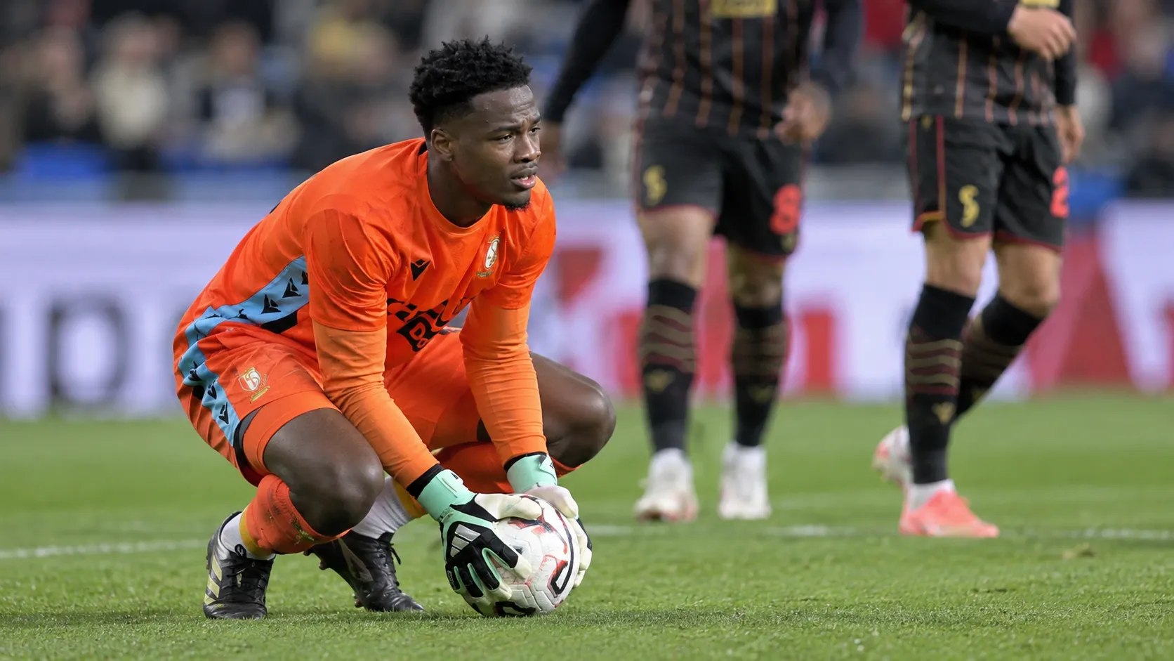 Matthieu Epolo van Standard hurkt op het veld met de bal in zijn handschoenen.