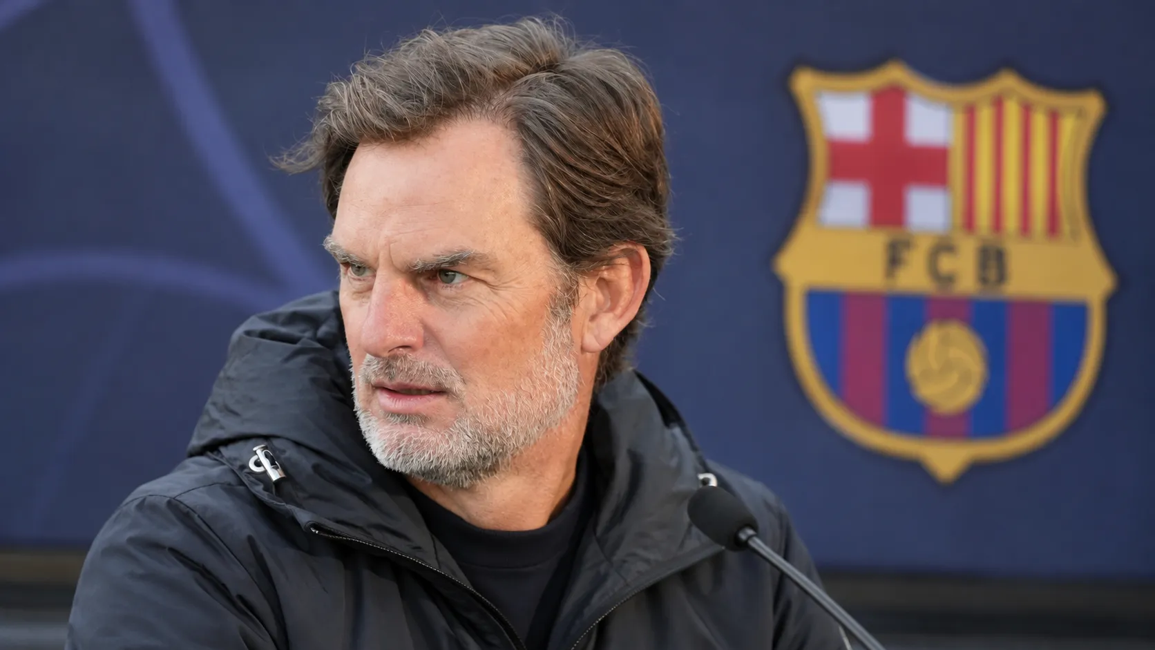 Ronald de Boer tijdens een interview met een subtiel Barcelona-embleem in de mediaomgeving.