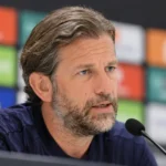 Rik De Mil tijdens een persmoment voor een voetbalachtergrond.