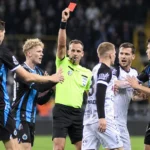 Scheidsrechter toont een rode kaart tussen spelers in zwart-blauwe en witte wedstrijdtenues.