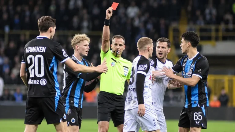 Scheidsrechter toont een rode kaart tussen spelers in zwart-blauwe en witte wedstrijdtenues.