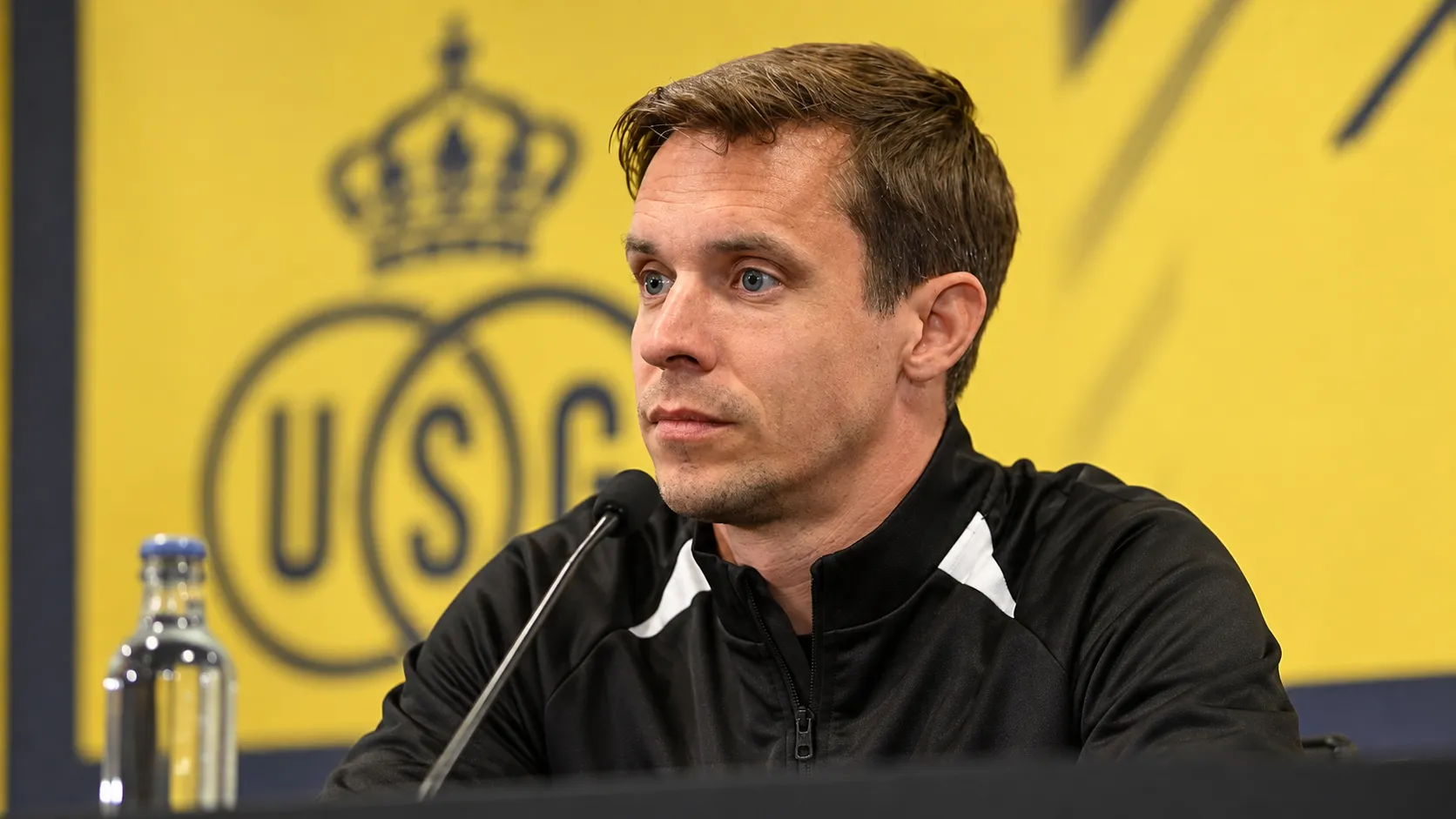 Een Union-coach in een zwarte trainingsjas tijdens een persmoment.