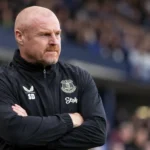 Sean Dyche in een donkere Everton-trainingsjas langs de zijlijn.