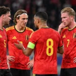 Vier Belgische spelers in rode shirts die zich tijdens een wedstrijd op het veld groeperen.