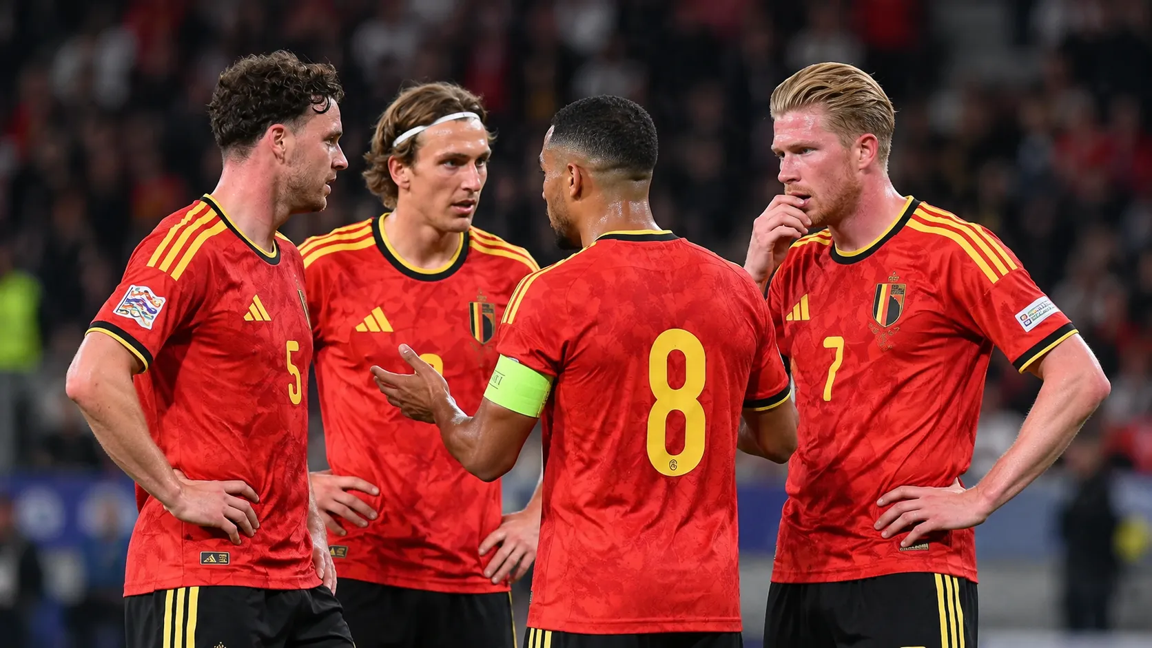 Vier Belgische spelers in rode shirts die zich tijdens een wedstrijd op het veld groeperen.