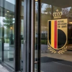 Glazen toegangsdeur van het KBVB-federatiegebouw met een fysiek geïntegreerd KBVB-embleem.