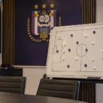 Lege tactische analysruimte van Anderlecht met een magneetbord en een clubembleem aan de wand.