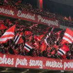 Een volle tribune met supporters van Standard die rood-wit-zwarte vlaggen zwaaien.