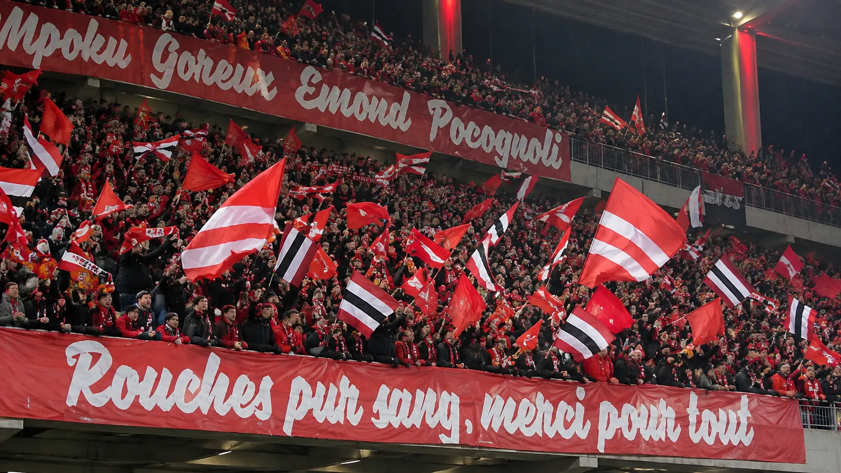 Een volle tribune met supporters van Standard die rood-wit-zwarte vlaggen zwaaien.