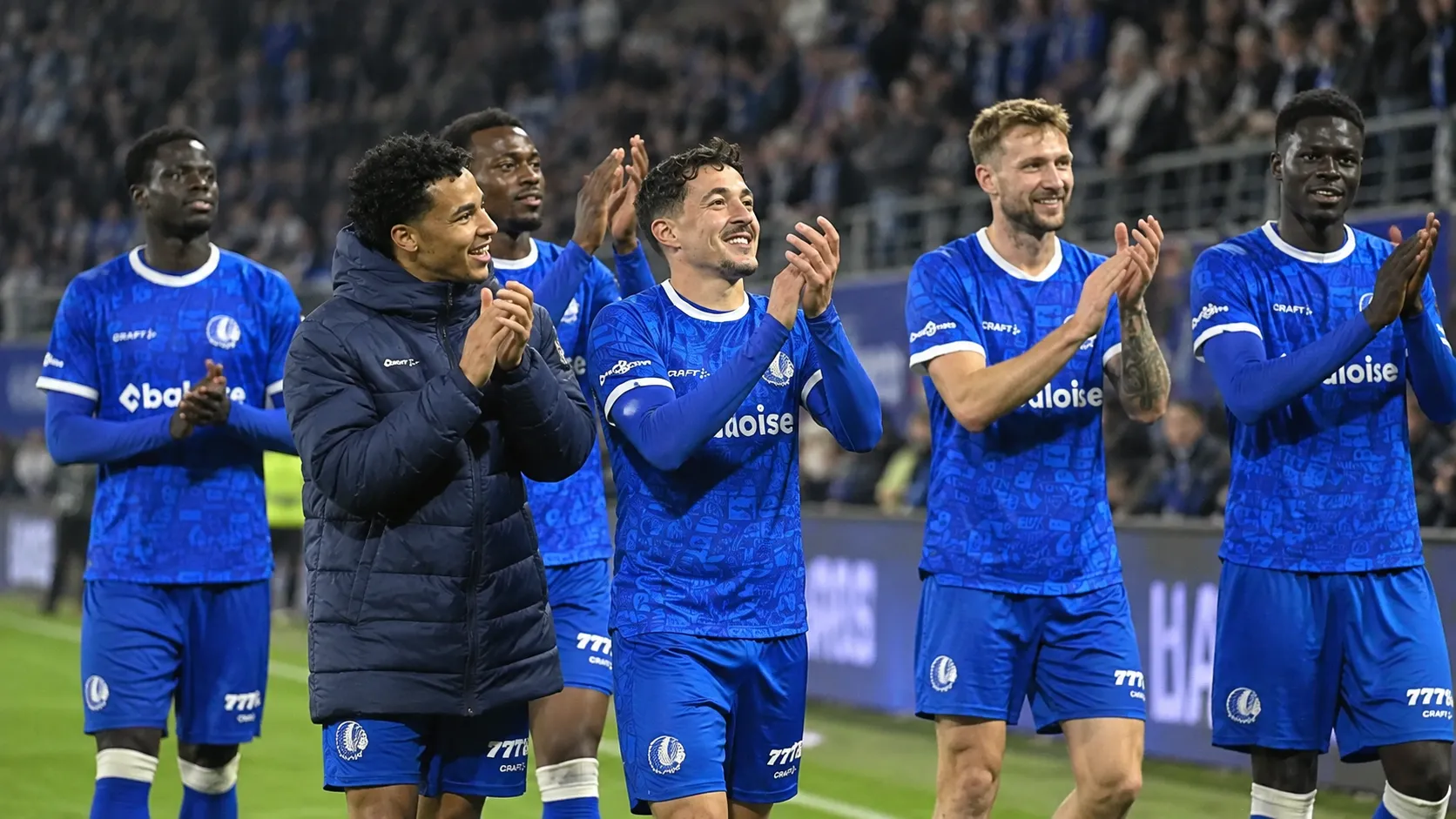 Een groep KAA Gent-spelers applaudisseert op het veld na een thuiswedstrijd.