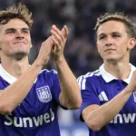 Twee spelers van Anderlecht applaudisseren na een wedstrijd in paarse shirts.