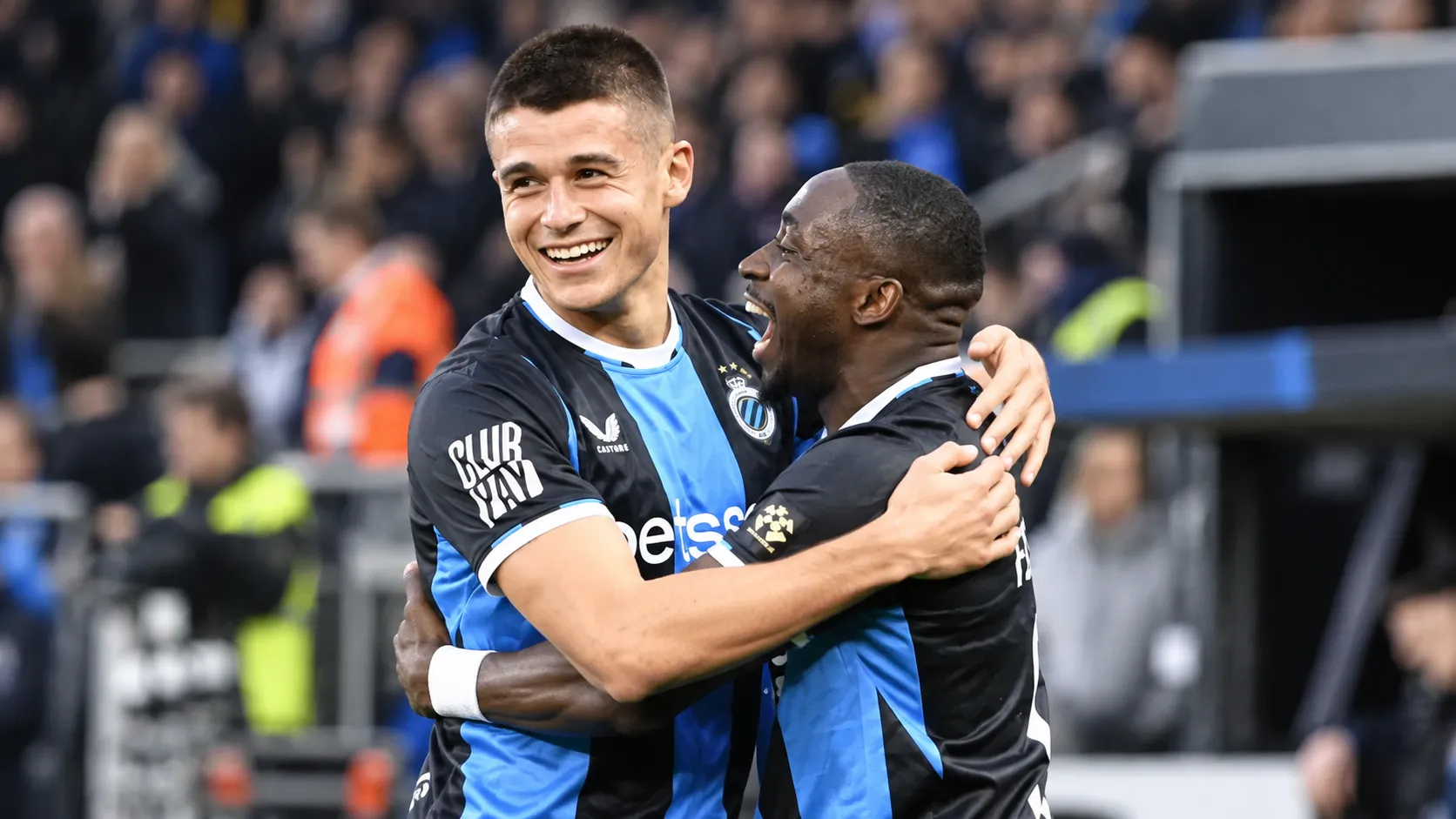 Twee voetballers in zwart-blauwe shirts vieren samen na een wedstrijd.
