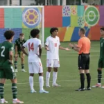 Jeugdspelers in witte en groene tenues staan met een scheidsrechter op het veld.