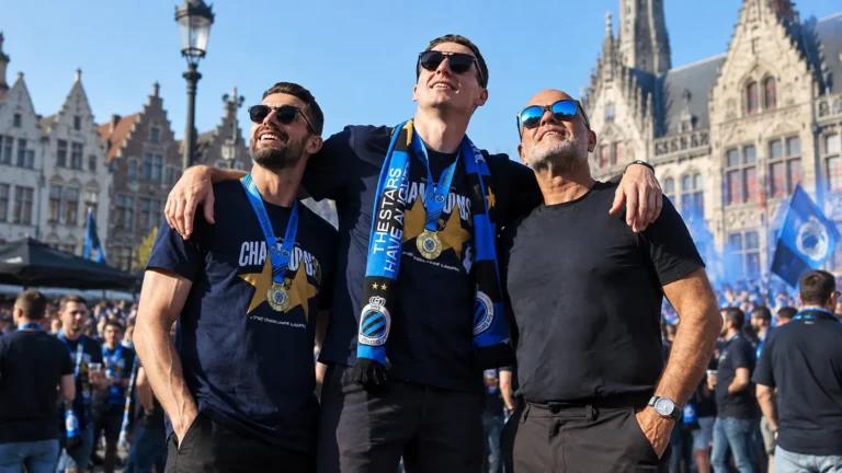 Een groep Club Brugge-supporters met blauw-zwarte sjaals op een stadsplein.