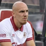 Een Antwerp-speler in een wit shirt met bordeaux details zit aandachtig in de dug-out.