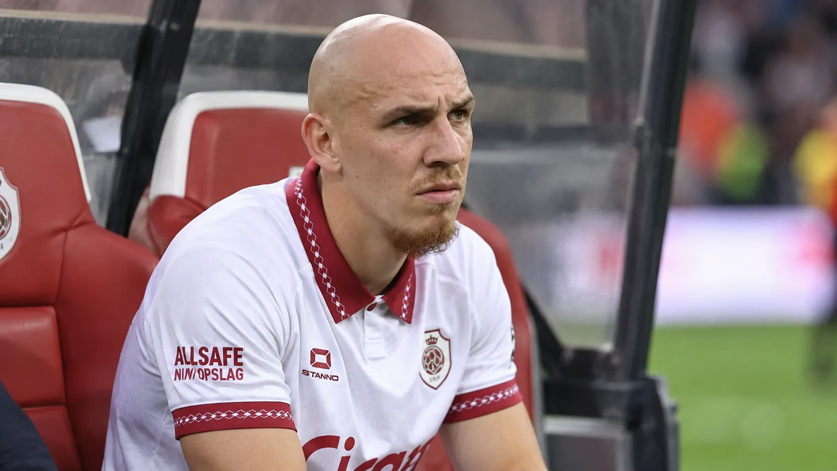 Een Antwerp-speler in een wit shirt met bordeaux details zit aandachtig in de dug-out.