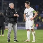 Een coach in zwarte jas spreekt na de wedstrijd op het veld met een speler van Cercle Brugge in wit tenue.
