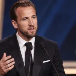 Harry Kane spreekt in een donker pak op het podium van de Gouden Bal.