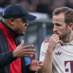 Een coach spreekt langs de zijlijn met een speler in een wit voetbalshirt.