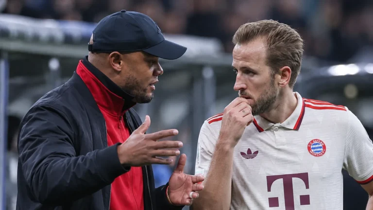 Een coach spreekt langs de zijlijn met een speler in een wit voetbalshirt.