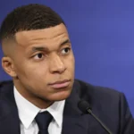 Kylian Mbappé in formele kleding tijdens een neutraal mediamoment.