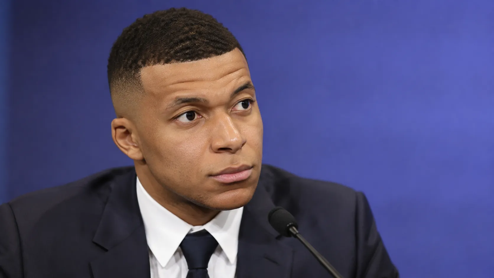 Kylian Mbappé in formele kleding tijdens een neutraal mediamoment.