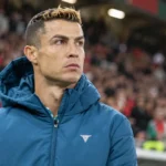 Cristiano Ronaldo in een blauwe gewatteerde jas langs de rand van een stadion.
