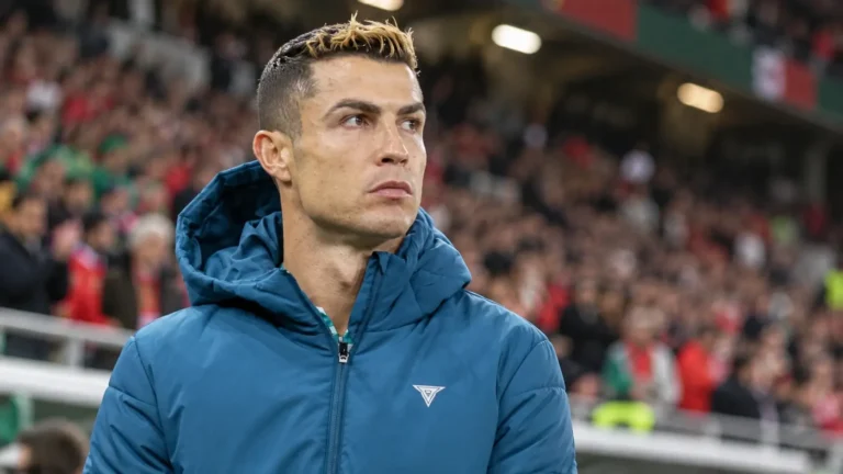 Cristiano Ronaldo in een blauwe gewatteerde jas langs de rand van een stadion.