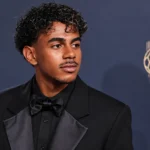 Lamine Yamal in zwart avondpak bij een perswand van de Ballon d'Or-ceremonie.