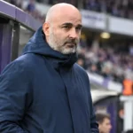 Een clubofficial in een donkere jas naast de dug-out van RSC Anderlecht.