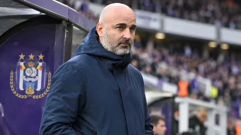 Een clubofficial in een donkere jas naast de dug-out van RSC Anderlecht.