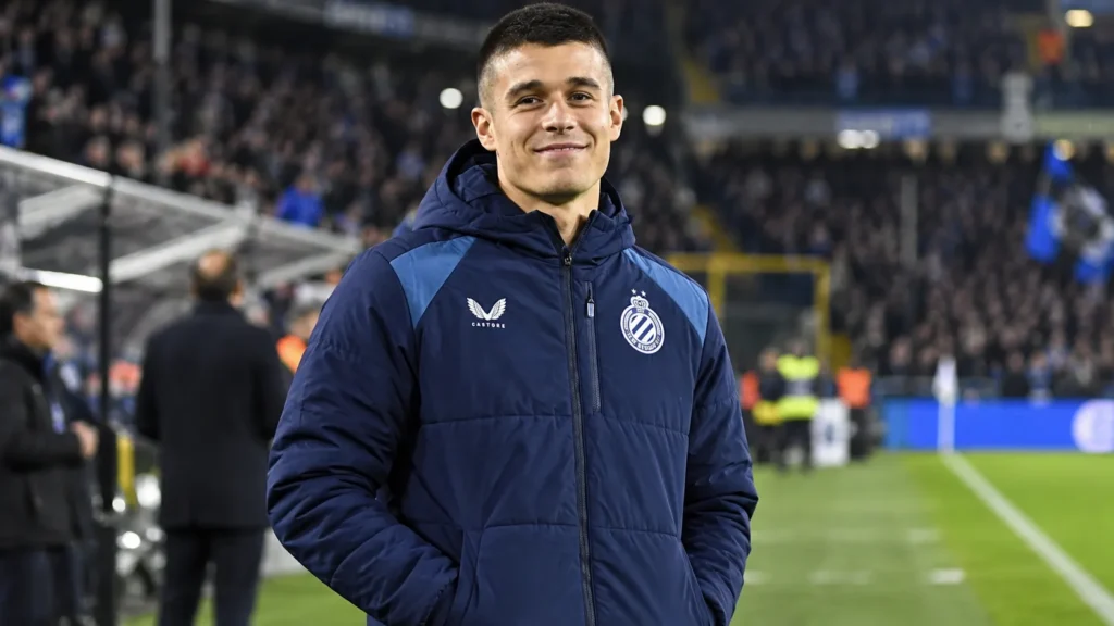 club-brugge-nicolo-tresoldi-januari-niet-te-koop Nicolo Tresoldi in een Club Brugge-jas langs de zijlijn van een gevuld stadion.